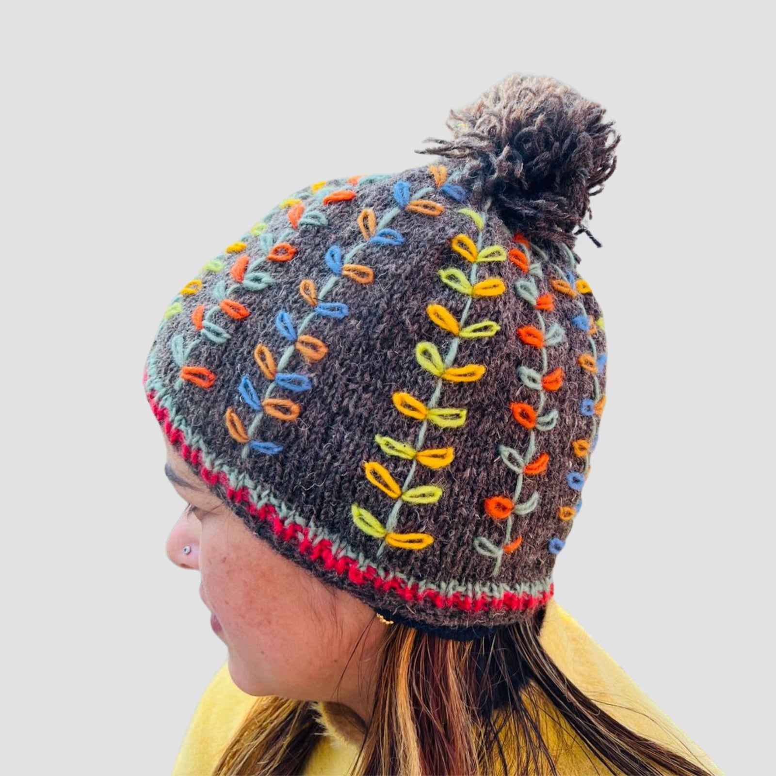 Woman wearing hand knitted grey beanie with colorful leaf embroidery Nepal