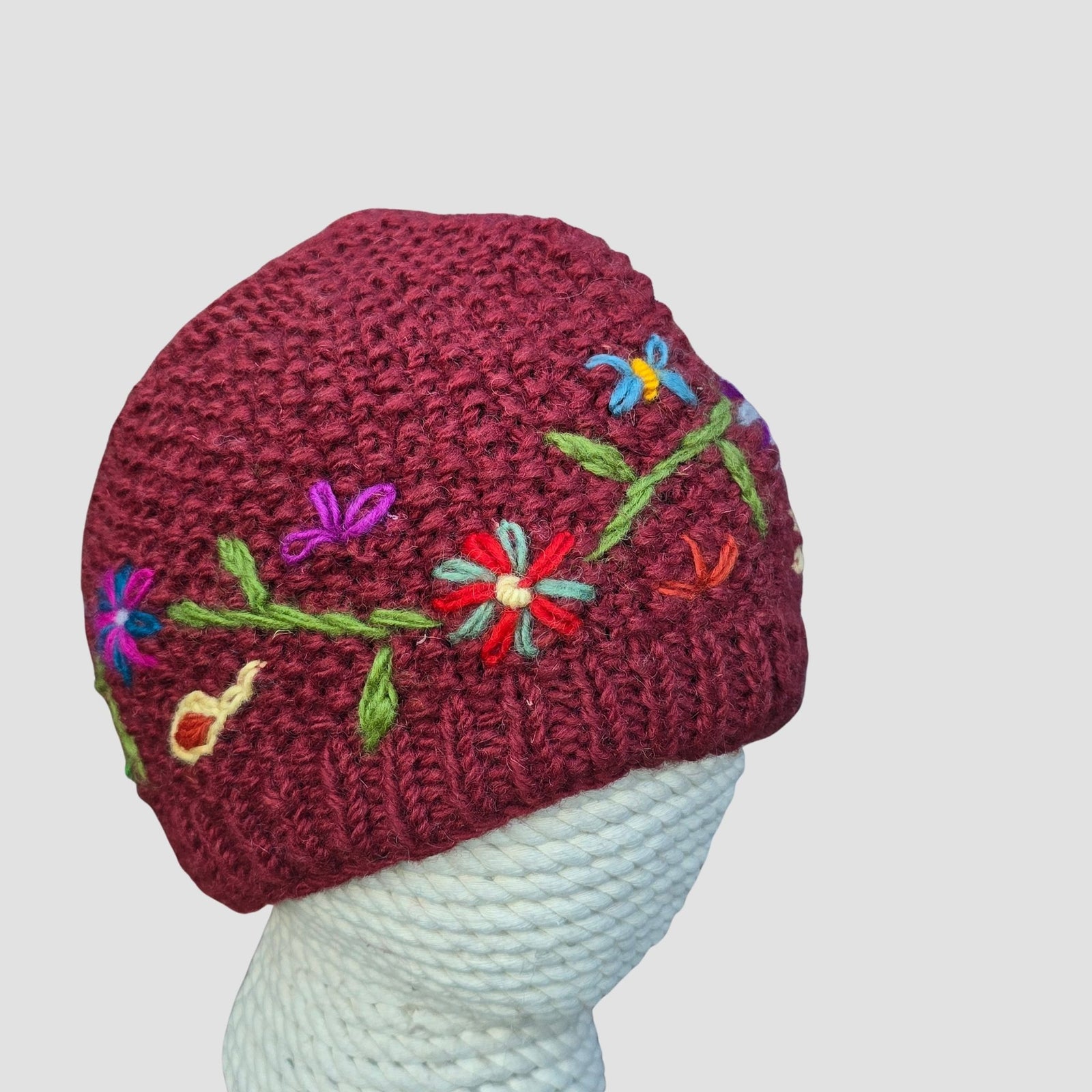 
Cranberry red hand knitted New Zealand wool beanie with scattered wildflower vine embroidery fleece lined handmade in Nepal on mannequin