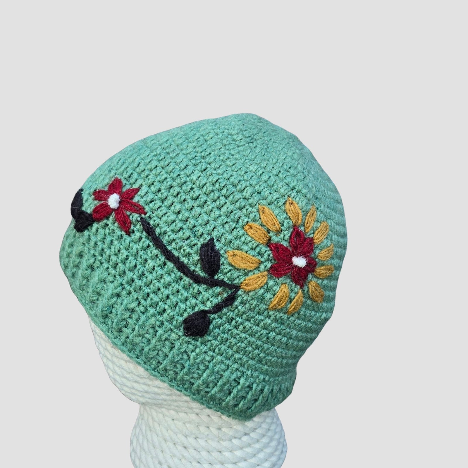 Sage green hand knitted New Zealand wool beanie with mustard sunflower and black stem botanical embroidery handmade in Nepal