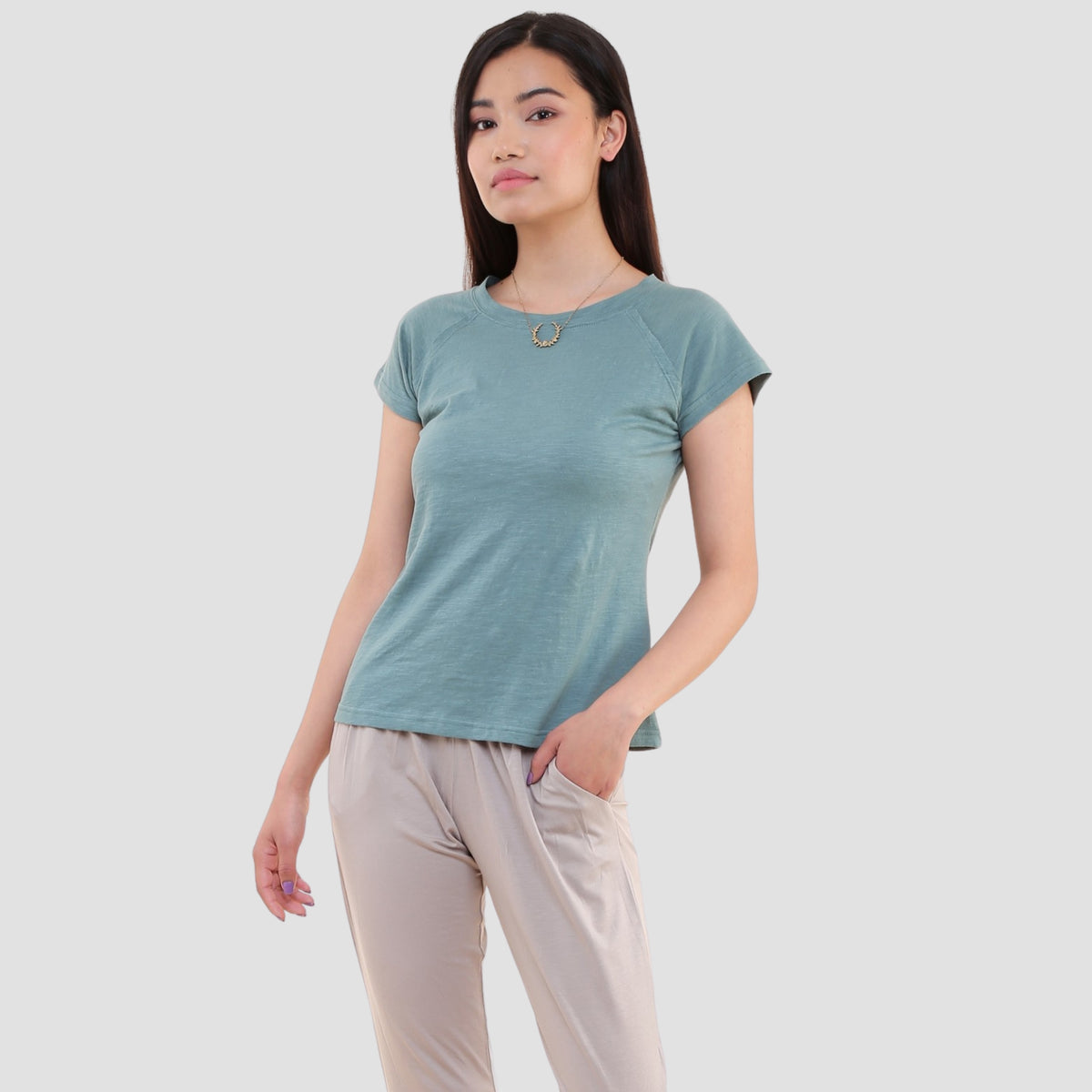 Woman wearing sage blue organic cotton short sleeve t-shirt with crew neck, paired with beige pants
